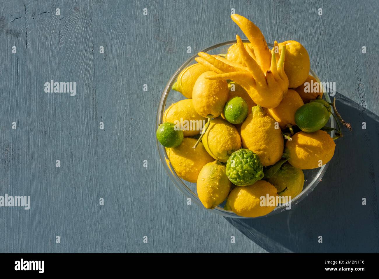 Various yellow and green type fresh ripe lemon fruits in a glass bowl. Group of organic lemons on sunny day. Pure antioxidant vitamin C. Natural food Stock Photo