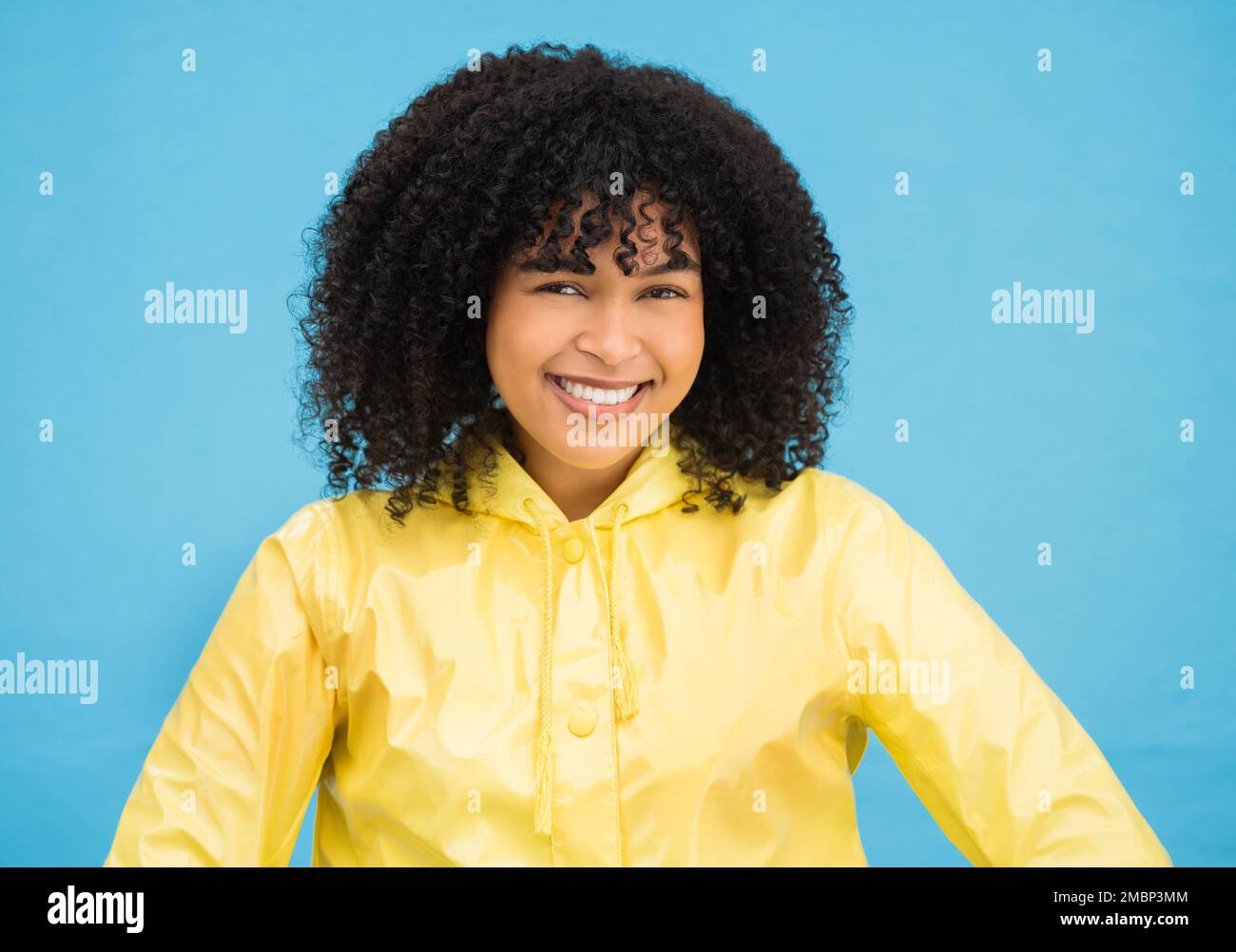 Black woman, smile and happy in portrait with fashion for winter, rain coat and beauty isolated on blue background. Happiness in studio, style and Stock Photo
