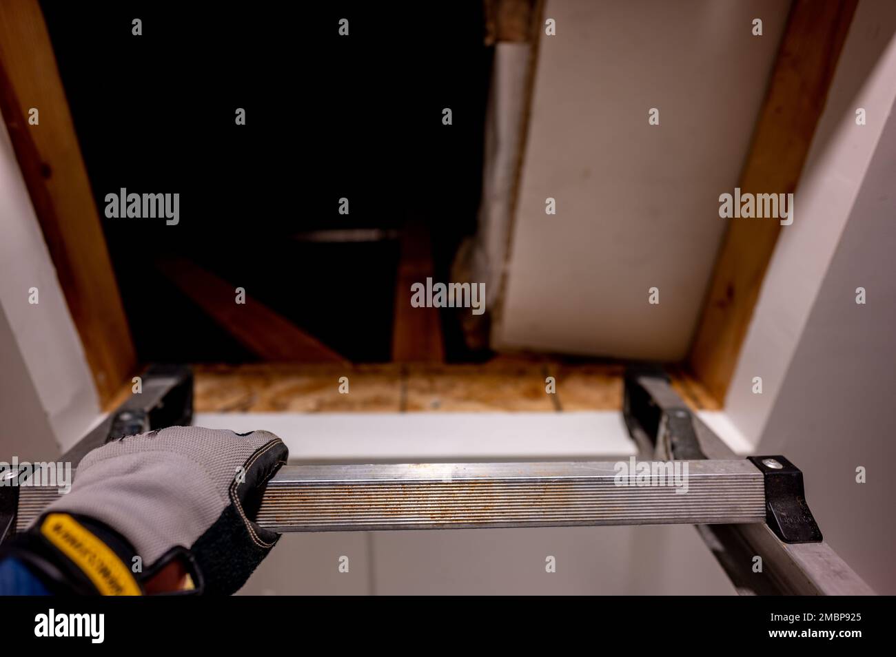 hand gripping the last rung on a ladder leading to an open attic Stock