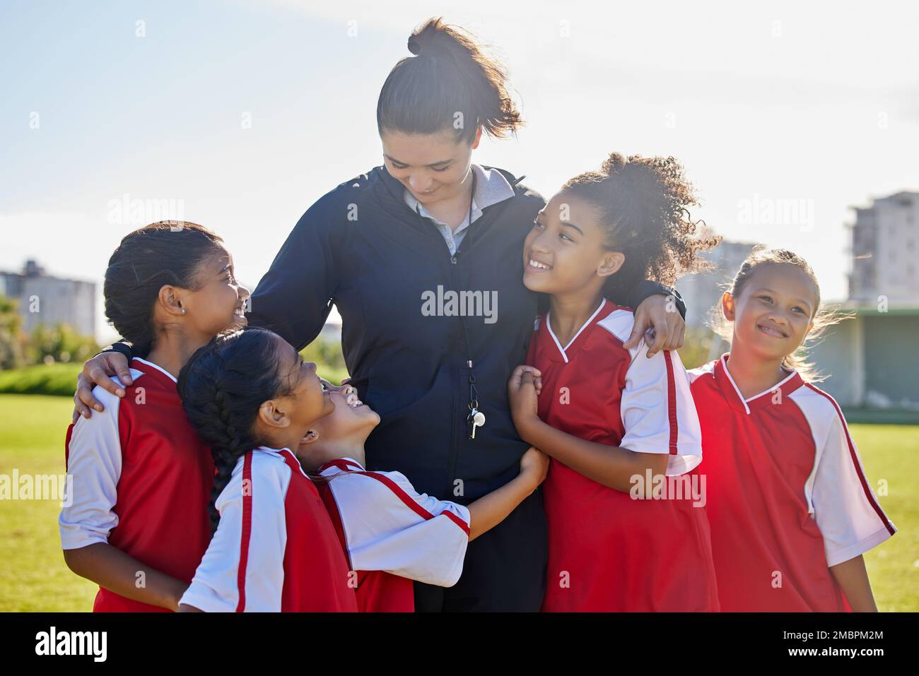 Girl football team, coach celebration and hug for success, teamwork and group diversity on grass pitch. Young female kids, soccer coaching and love Stock Photo