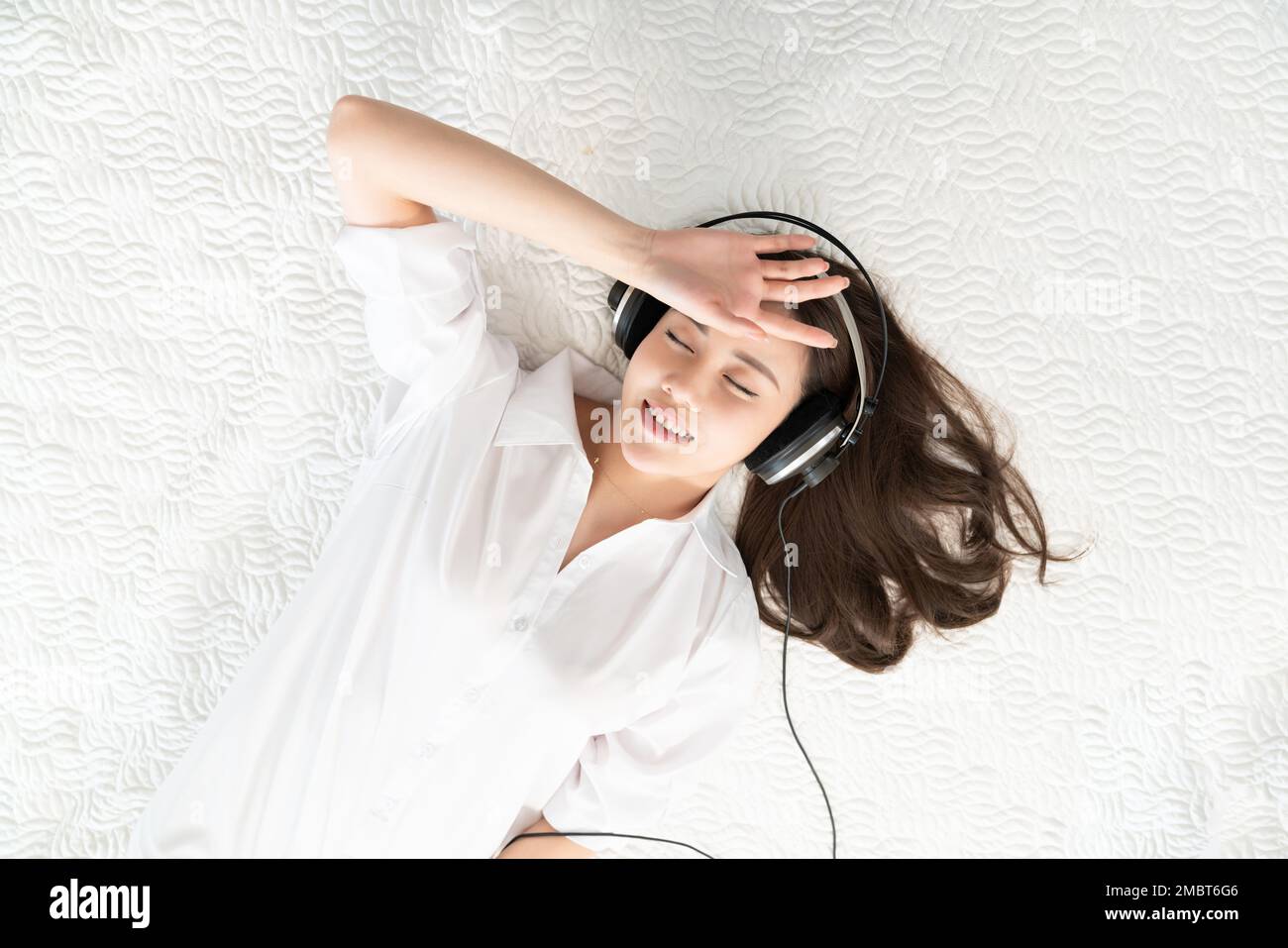 A young woman lying in bed listening to music Stock Photo - Alamy