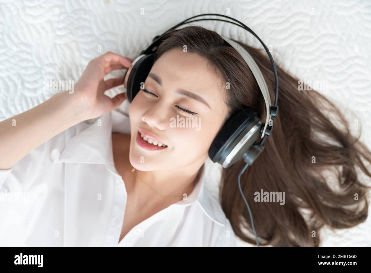 A young woman lying in bed listening to music Stock Photo - Alamy