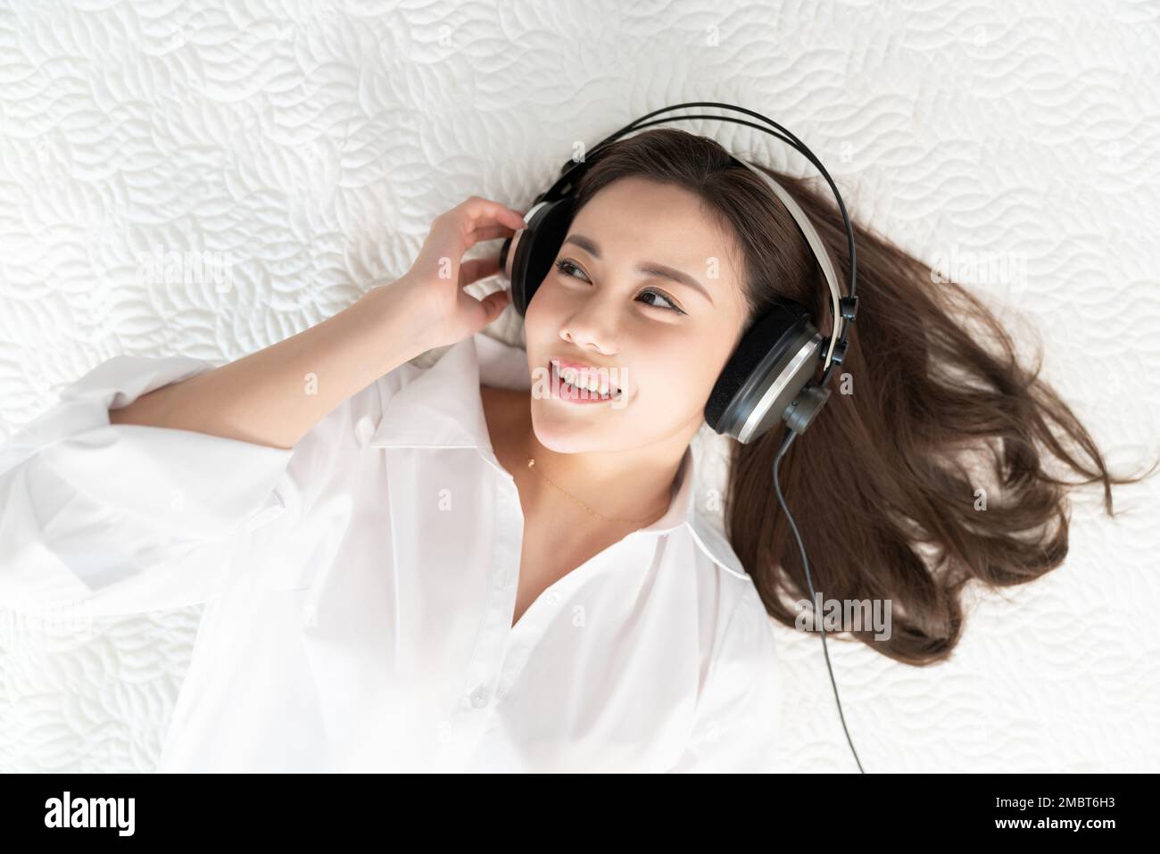 A young woman lying in bed listening to music Stock Photo - Alamy