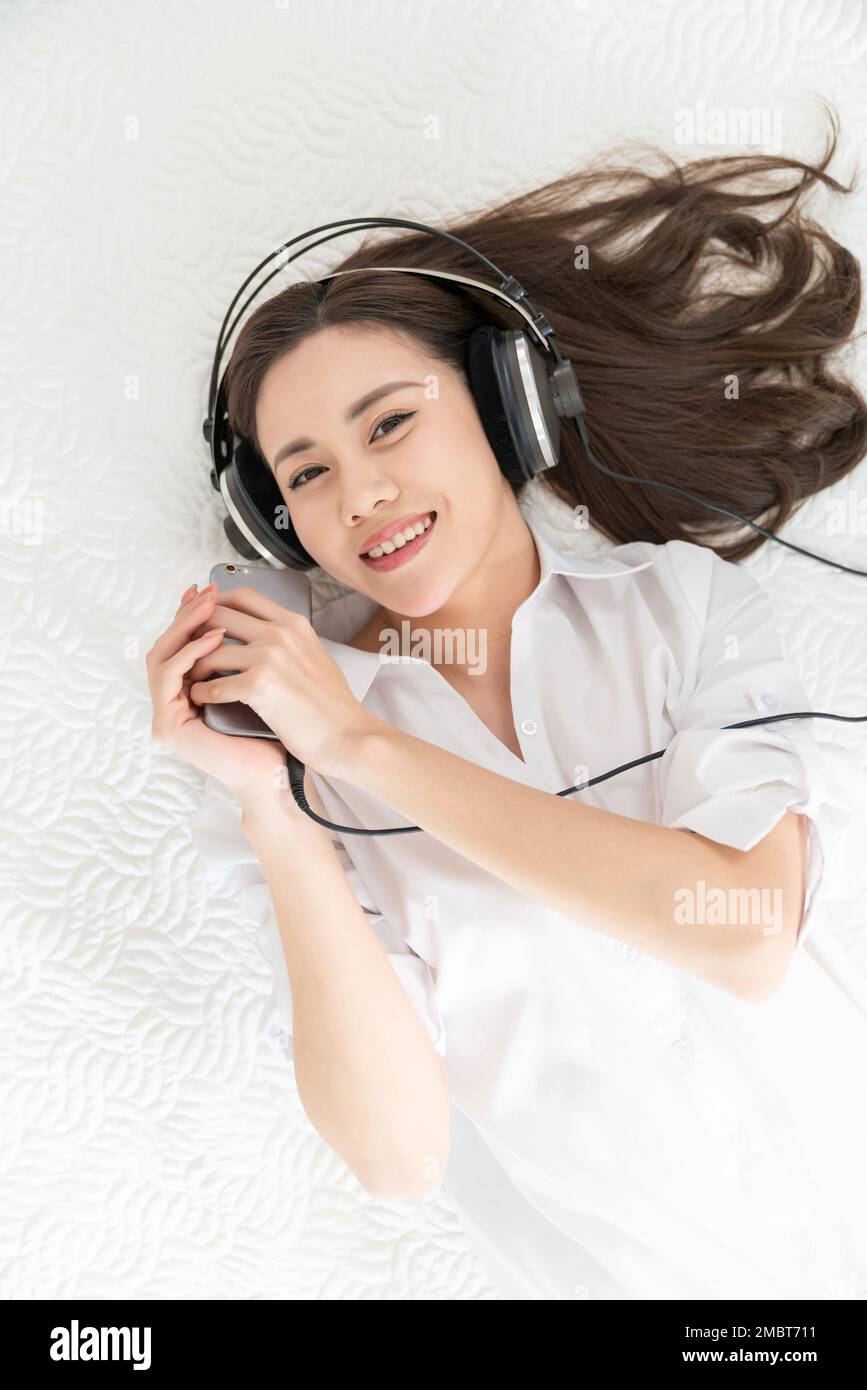 A young woman lying in bed listening to music Stock Photo - Alamy
