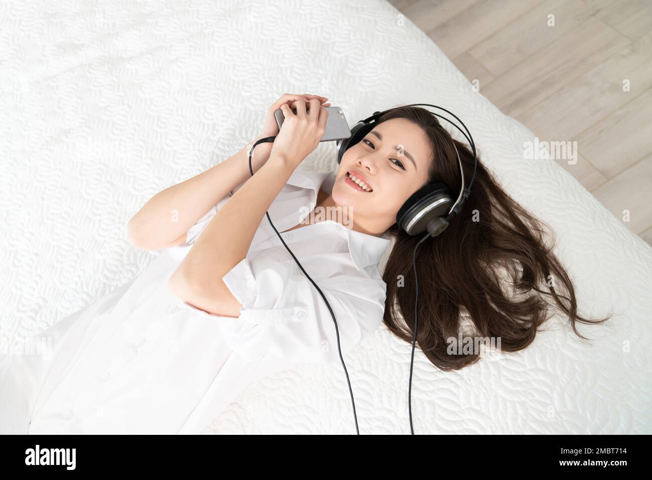 A young woman lying in bed listening to music Stock Photo - Alamy