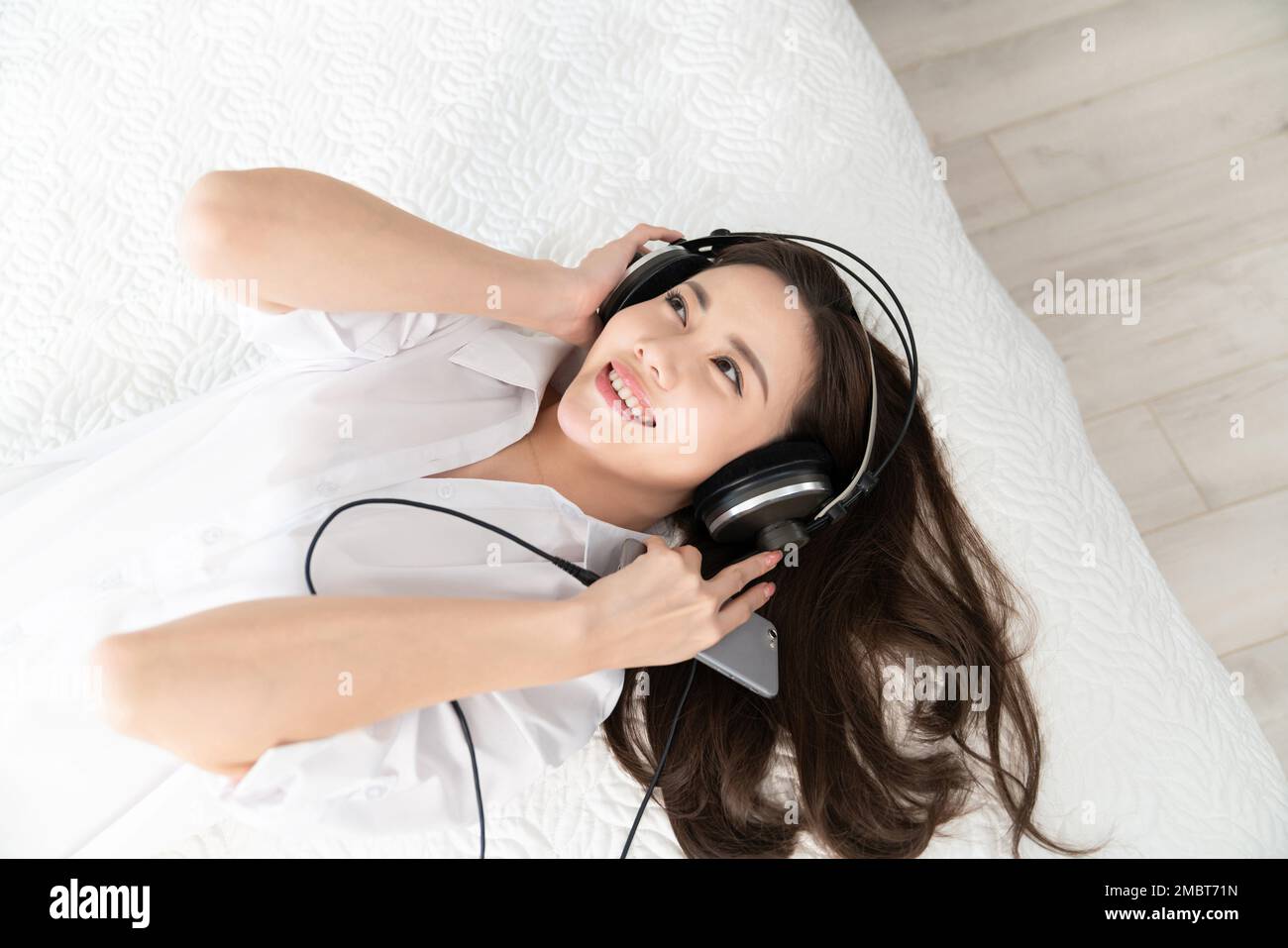 A young woman lying in bed listening to music Stock Photo - Alamy