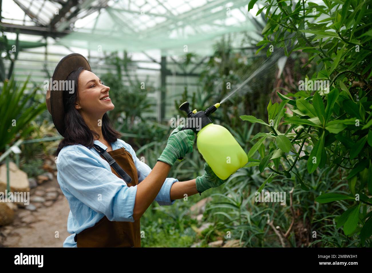 Young woman gardener caring plants treating flowers with chemicals