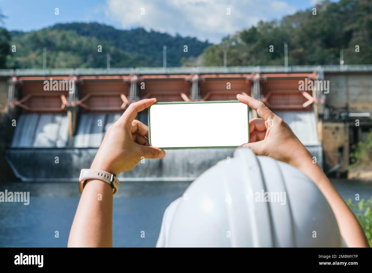 Environmental engineer using mobile phone to take picture with white screen against dam background. Water and ecology concept. Stock Photo