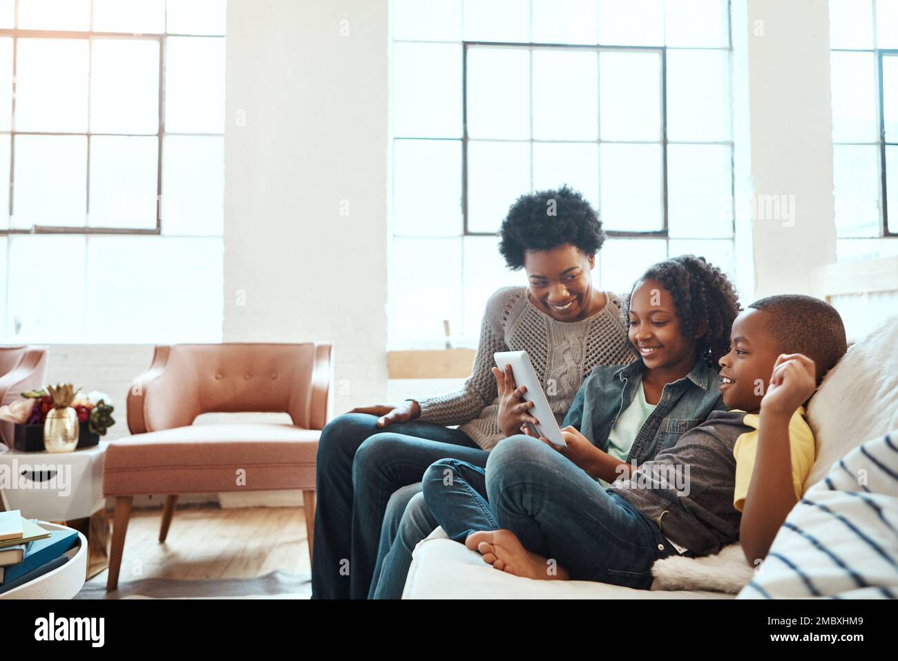 Family with tablet, watch and relax at family home together, spending quality time together with technology. Black people, mother and children on sofa Stock Photo