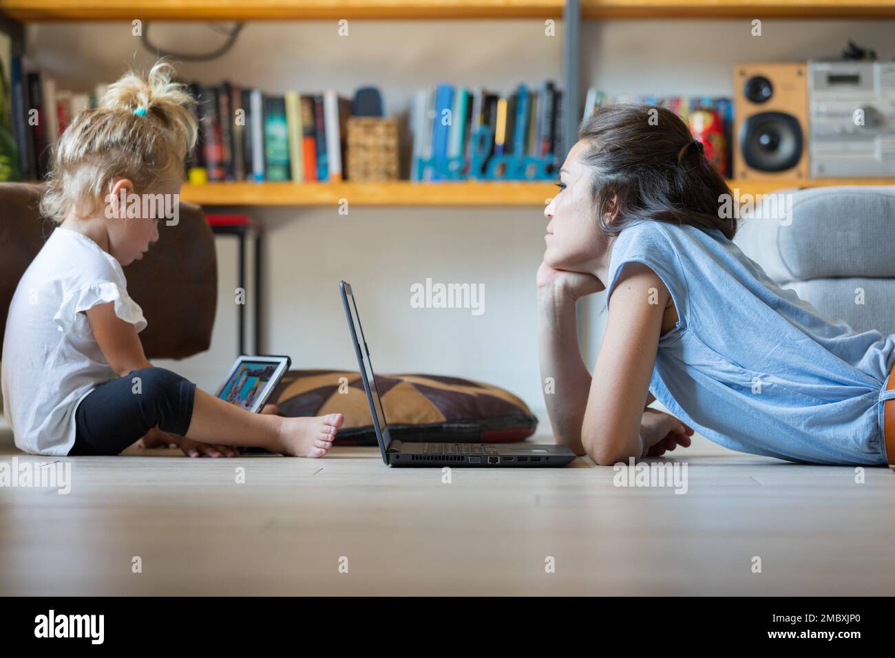 The mother carefully observes her child using a digital tablet. She supports and accompanies her in her growth. She uses the laptop and they stand tog Stock Photo