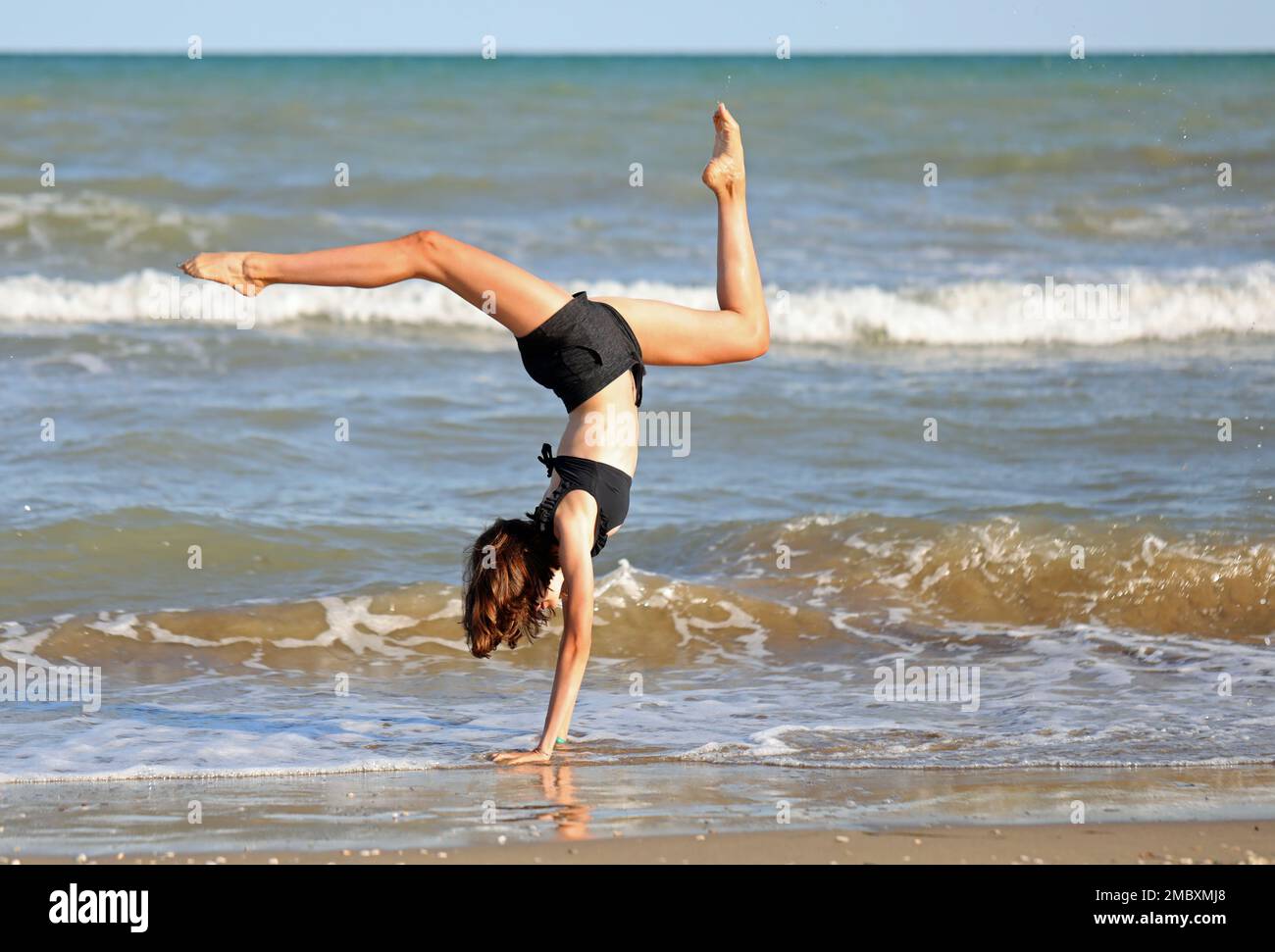 young barefoot girl in black swimsuit from rhythmic gymnastics exercises on the seashore Stock Photo