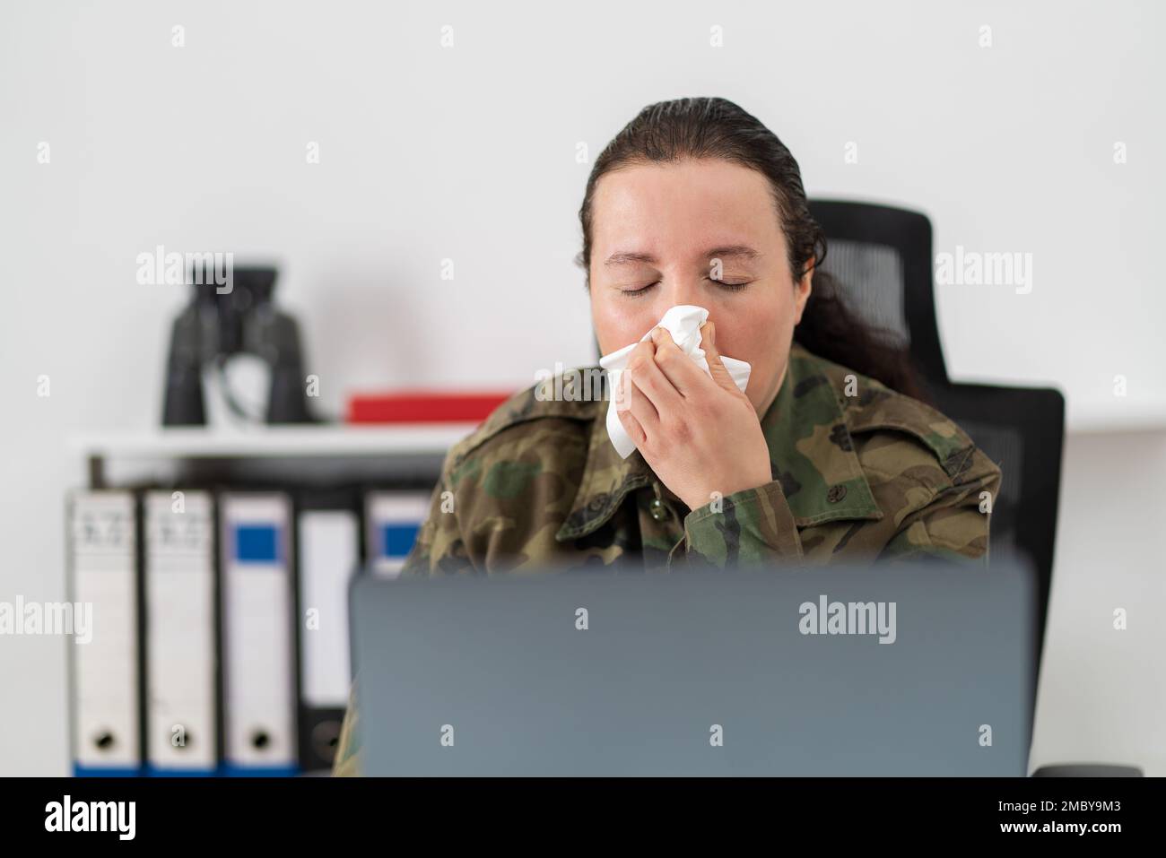 Shot of a female soldier blowing her nose with a tissue at work Stock Photo
