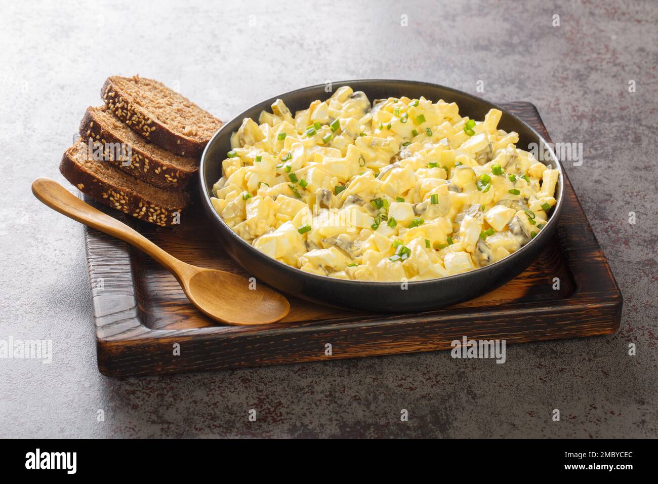 Eiersalat is a creamy German egg salad with cubes of crisp apple and crunchy sour pickles. closeup on the wooden board on the table. Horizontal Stock Photo