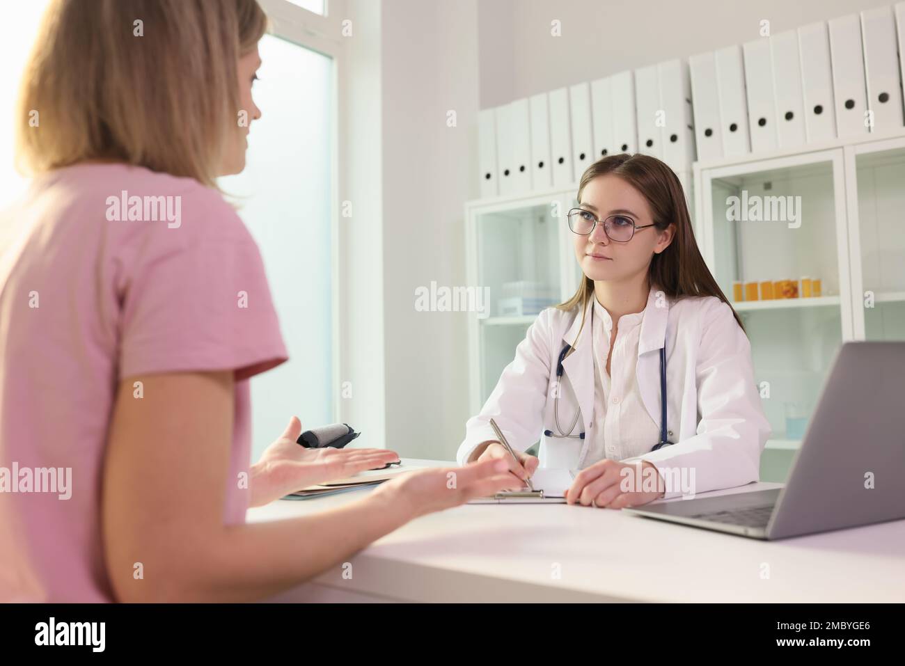 Doctor communicating with female patient in clinic and listening to her complaints Stock Photo