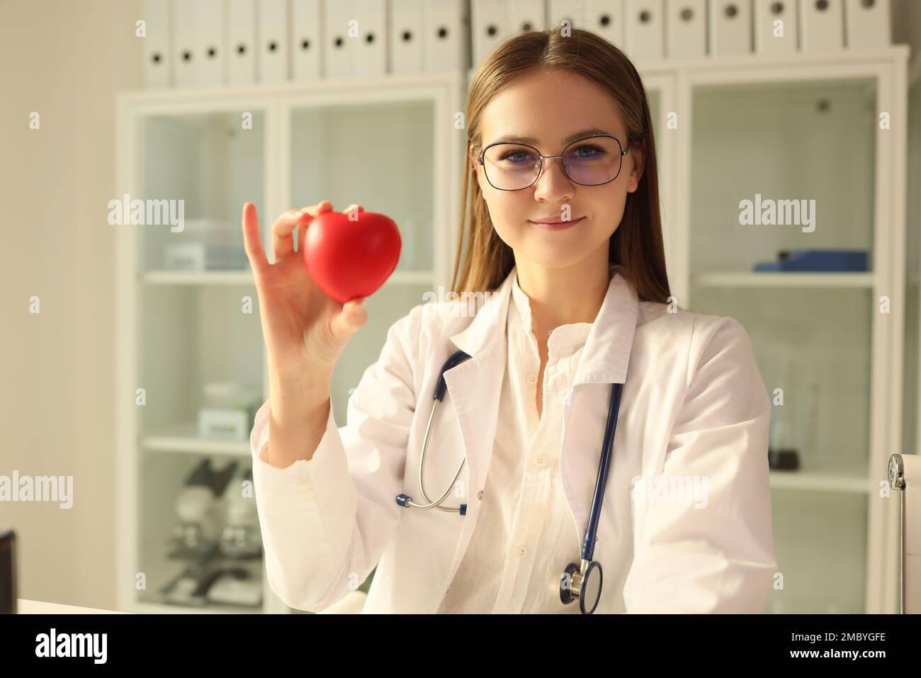 Doctor cardiologist holding red toy heart in clinic Stock Photo