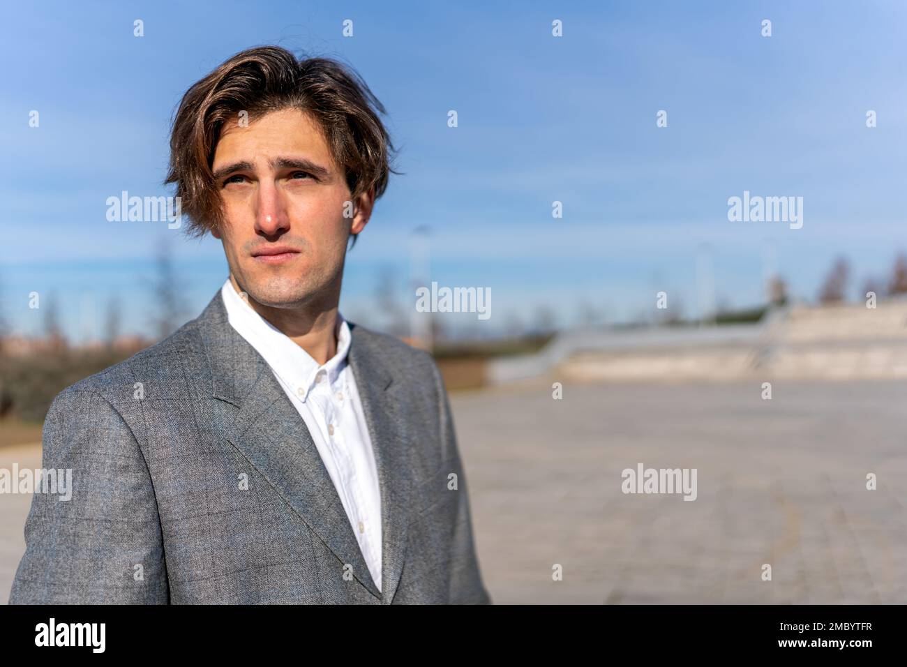 Thoughtful businessman wearing classy suit looking away while standing on street against blue sky Stock Photo