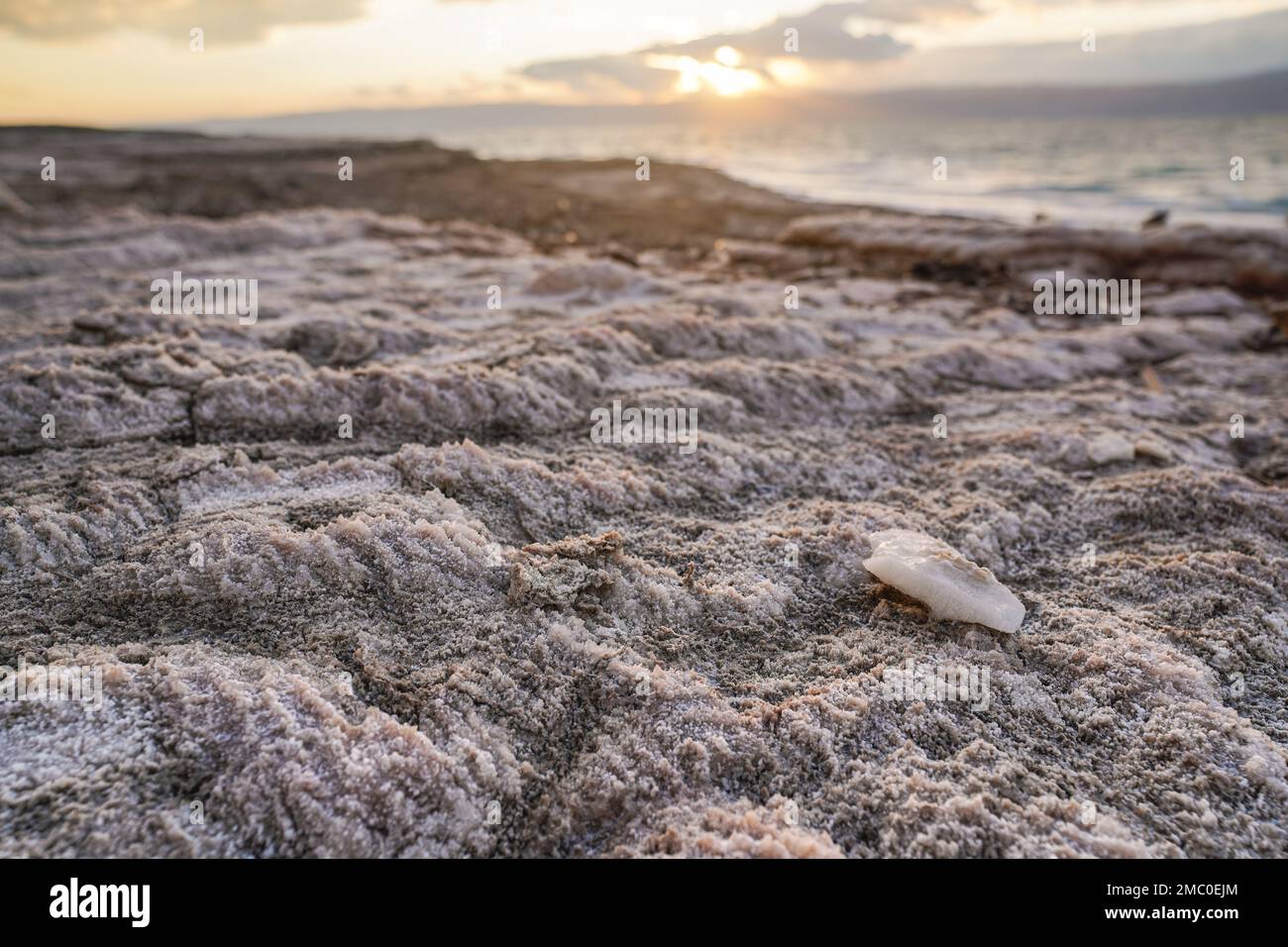 Sand and stones covered with crystalline salt on shore of Dead Sea, clear water background Stock Photo