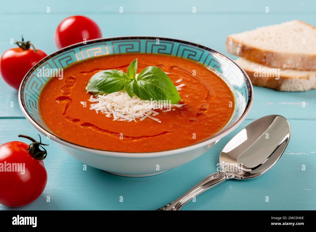 Hot tomato soup and spoon over turquoise wooden table. Homemade soup of pureed tomatoes with grated parmesan and fresh basil. Healthy vegetarian dish. Stock Photo