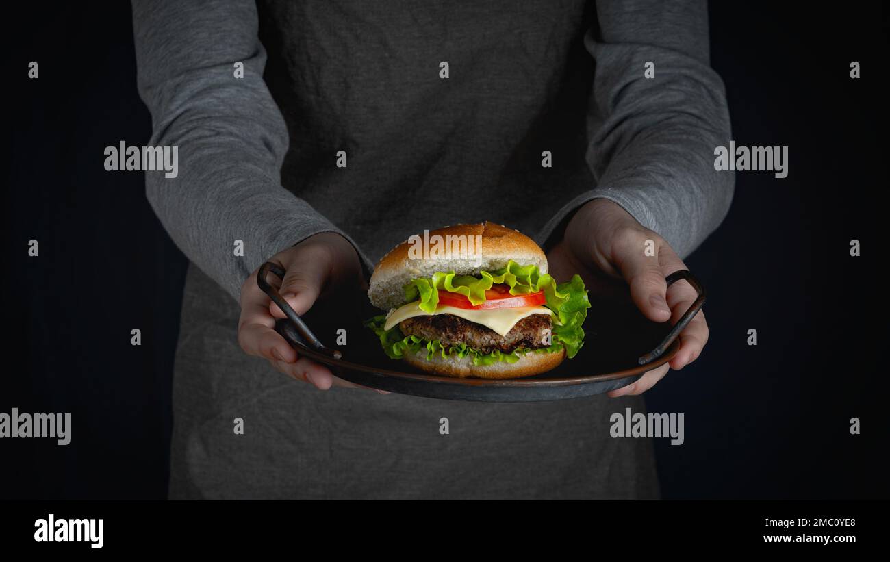 Woman in apron holding in her hands a tray with burger. Stock Photo