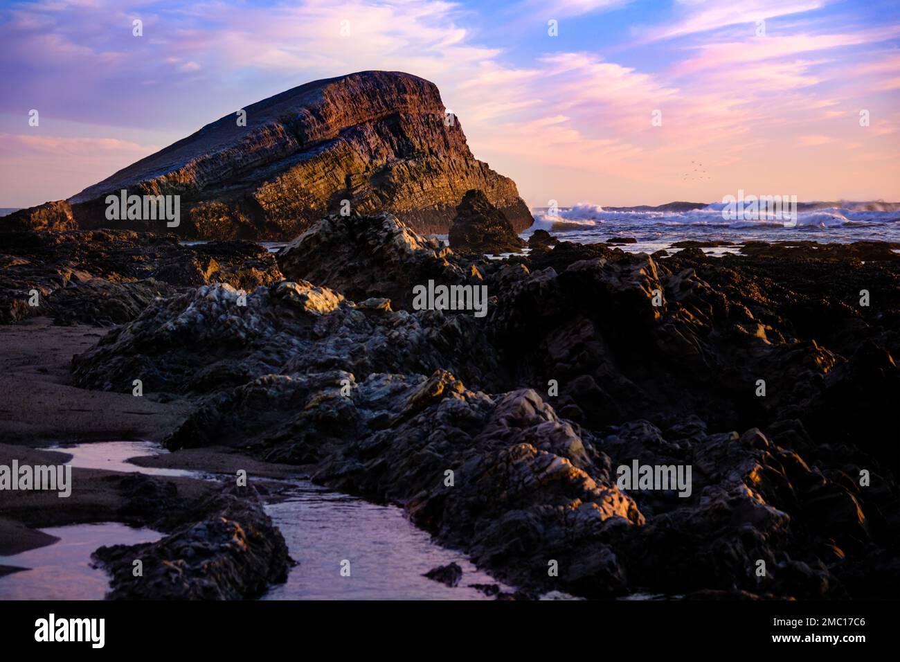 A beautiful rocky shore of the sea during purple sunset Stock Photo - Alamy