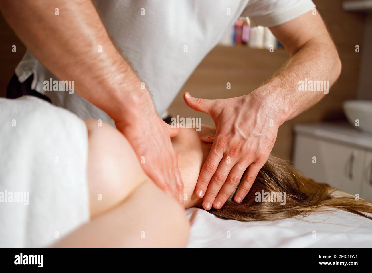 Close-up view of the masseur hands giving a neck and head massage to a young woman Stock Photo