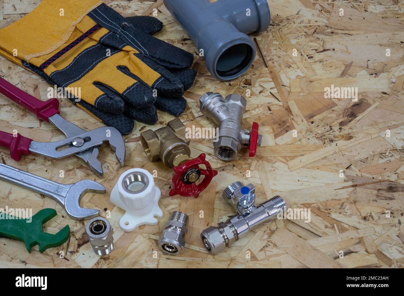 Plumbing tools, parts, pipeline components and gloves on the background of a construction OSB plate. Place for text or logo. Stock Photo