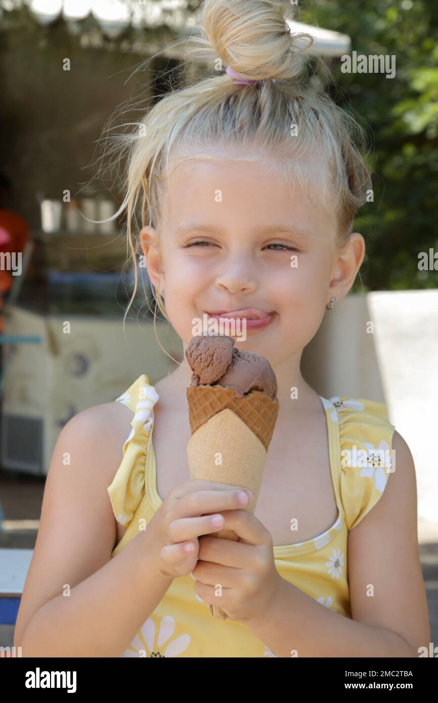 Happy little girl eating tasty fresh ice cream cone on sunchairs