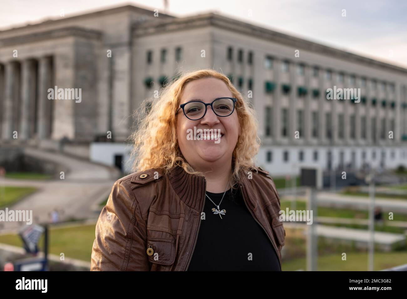 Portrait of a blonde and curly plus-size woman looking at camera while smiling in a University background Stock Photo