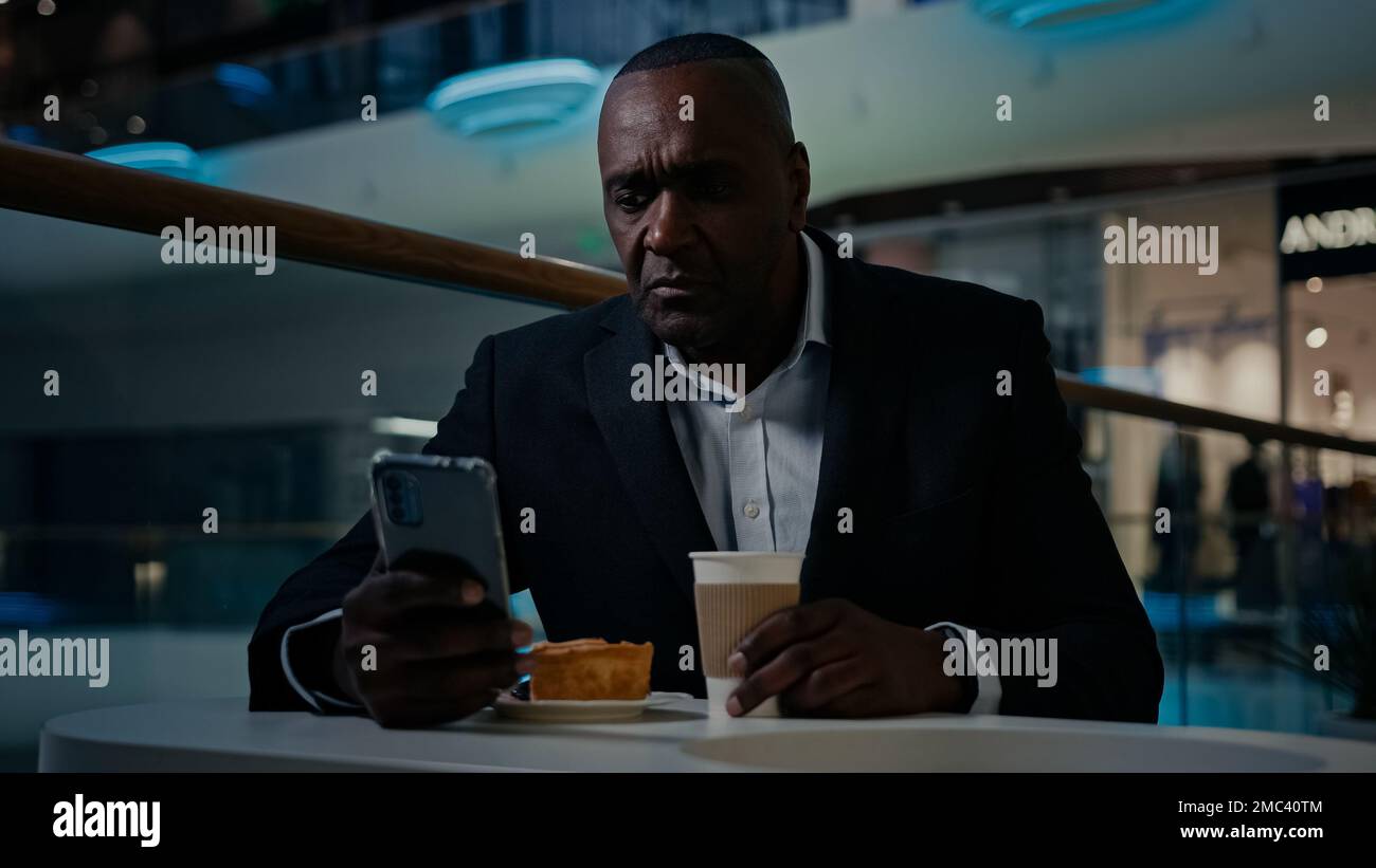 African American adult middle-aged businessman 50s ethnic man male employer entrepreneur sitting at table in cafe drink coffee drinking tea browsing Stock Photo