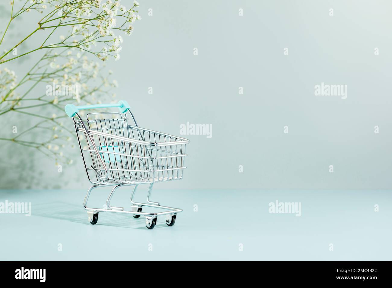 Shopping cart or trolley on blue background with white flowers and copy space. Spring season sale, spring shopping in supermarket concept Stock Photo