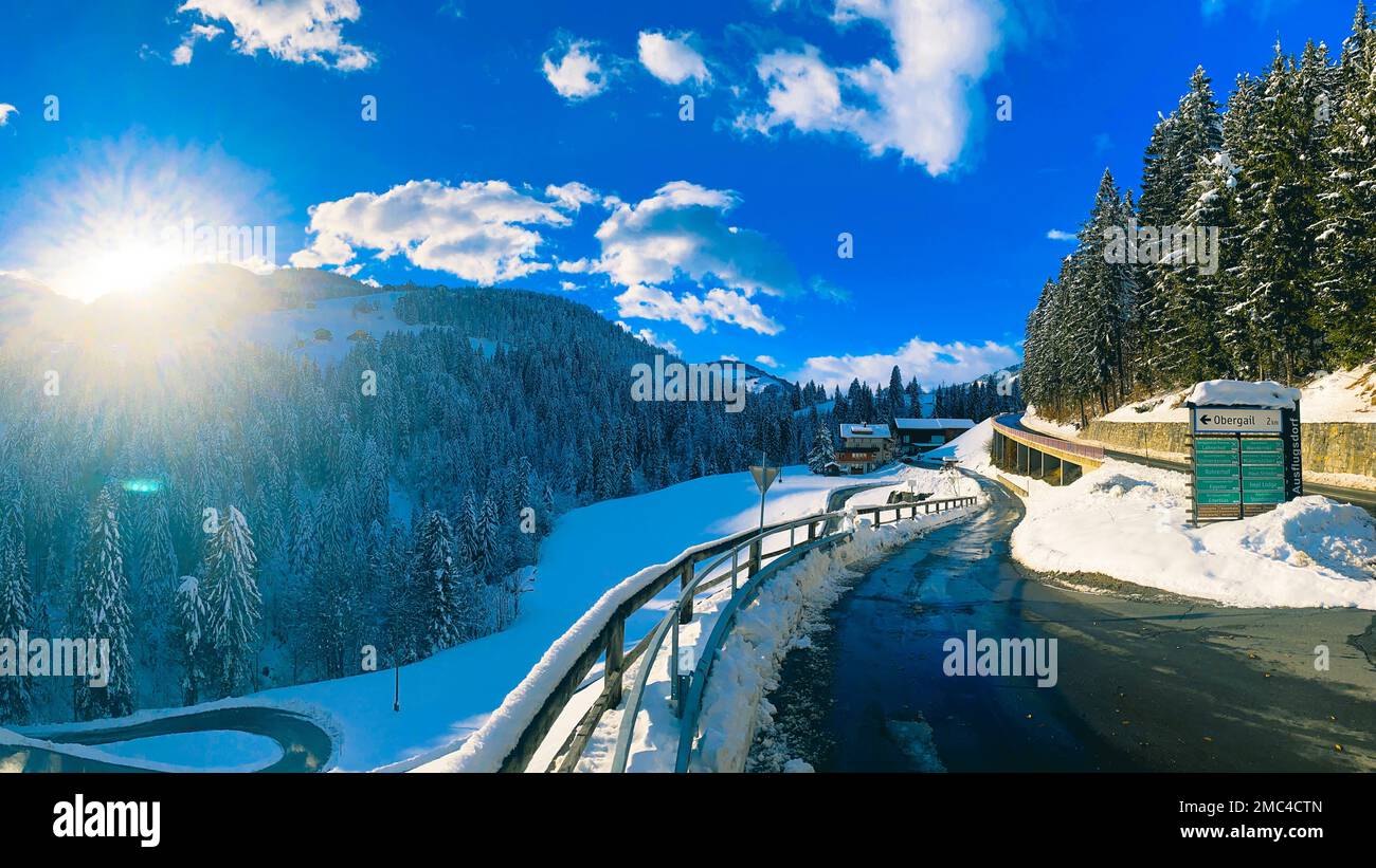 The empty road surrounded by woods and mountains on a sunny winter day. Austria. Stock Photo