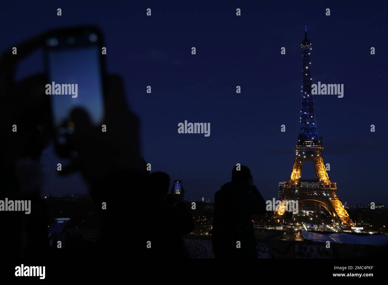 People photograph the Eiffel Tower, lighted with the colors of Ukraine