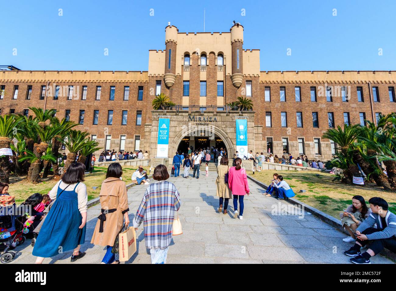 People walking to the main entrance of the imposing Miraiza building, containing shops and restaurants at Osaka castle in the springtime. Blue sky. Stock Photo