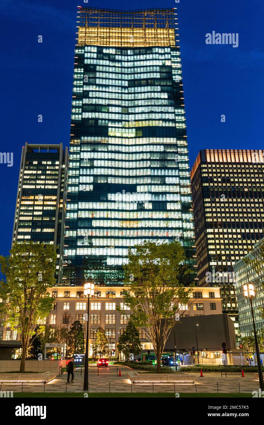 The KITTE Marunochi biulding with the JP Tower against a dark blue night sky seen from Marunouchi Ekimae Square. Illuminated with trees in front. Stock Photo