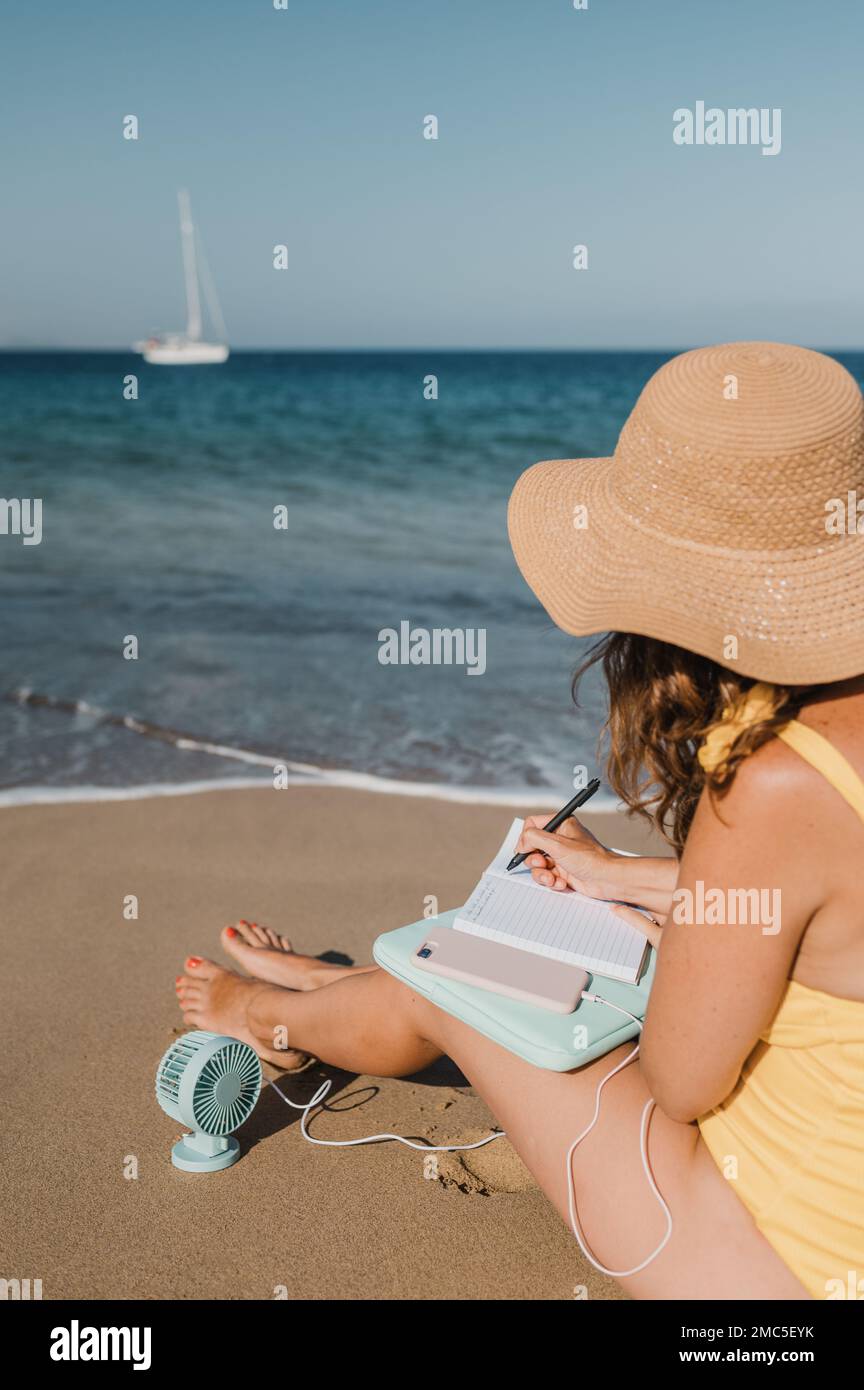 Anonymous woman writing in notebook on seashore Stock Photo