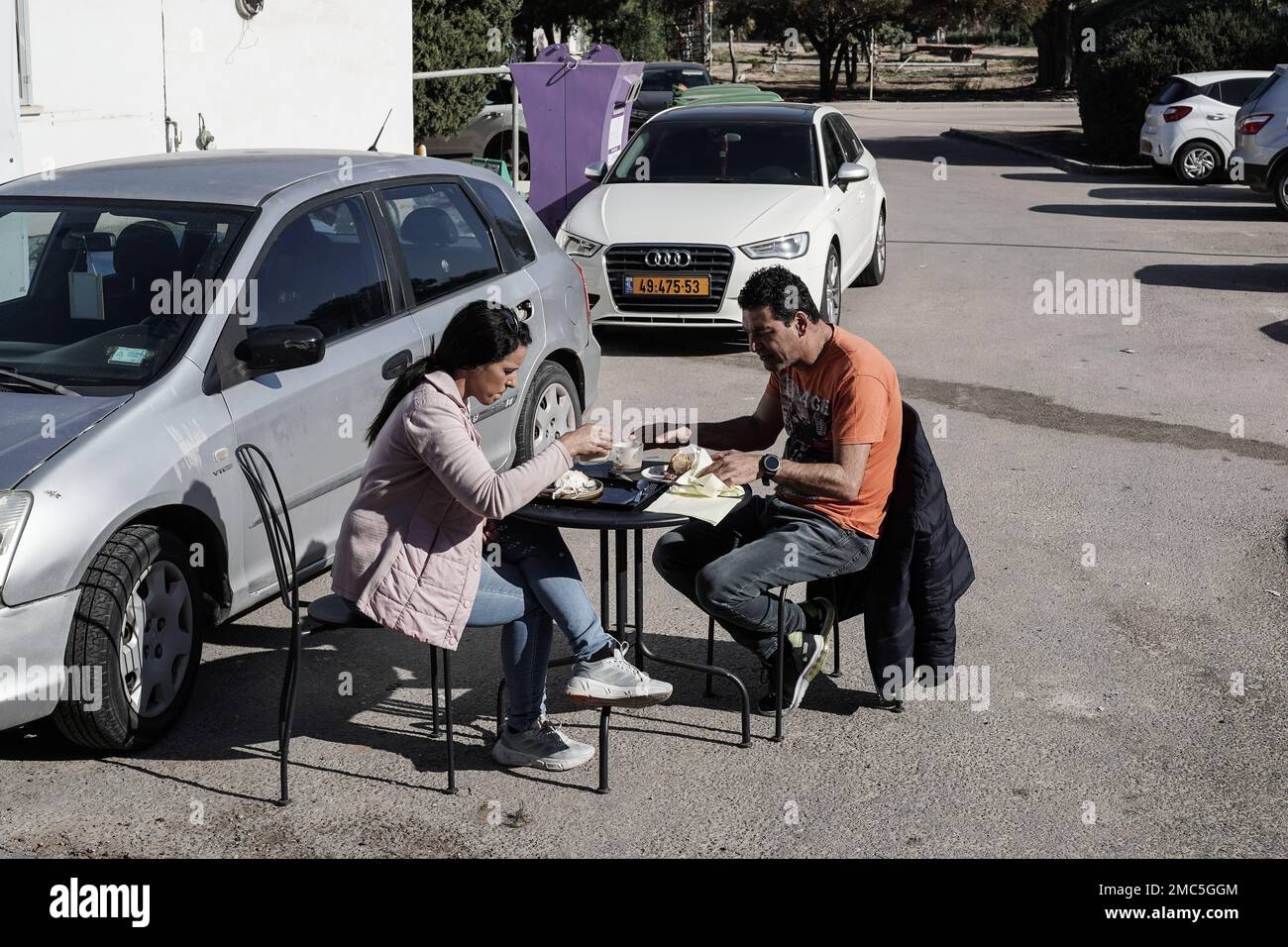A young couple enjoys breakfast and soaking in the January sun in a parking lot at Kibbutz Erez. Stock Photo