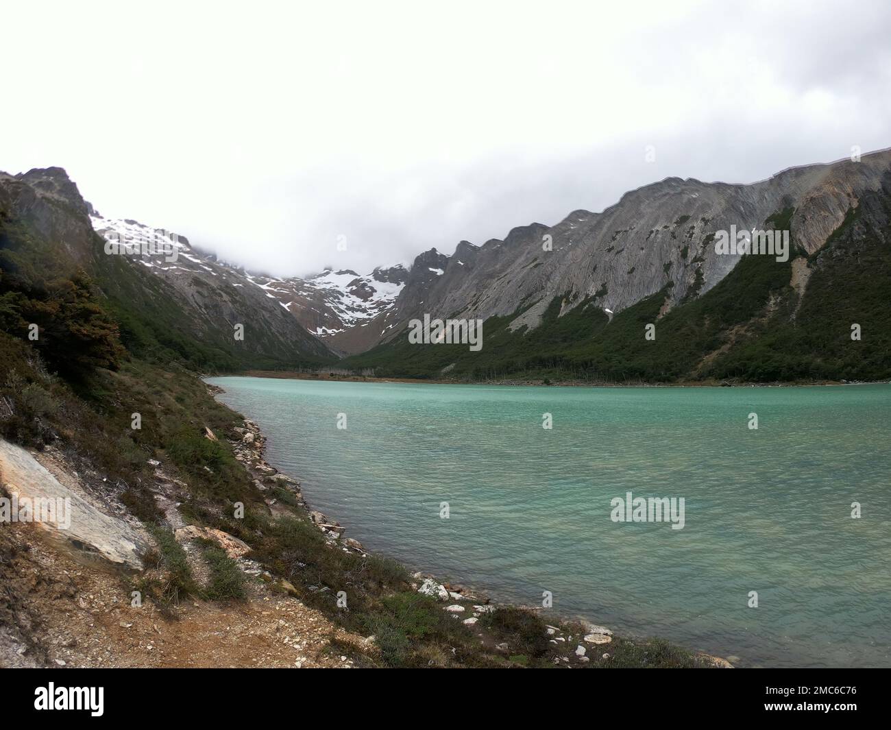 A lake surrounded by steep rocky mountains on a foggy day Stock Photo ...