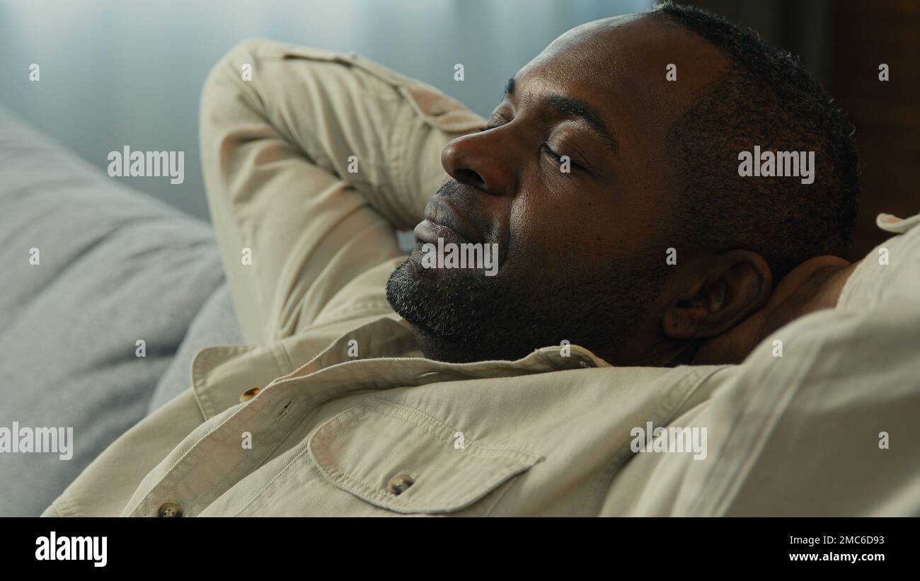 Headshot calm relaxed happy african american man relax resting on couch enjoying calmness sleepy lazy male dreamer dozing on comfortable sofa in Stock Photo