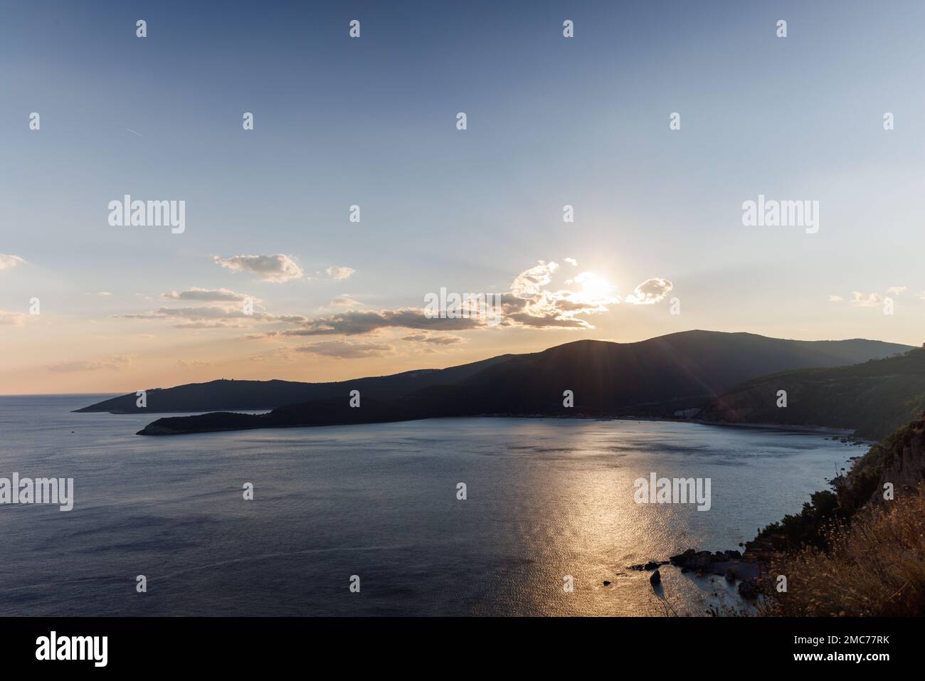 Dazzling sun in the evening sky illuminates all the peaks of the Balkan Montenegrin mountains and the coast of Kotor Bay Stock Photo