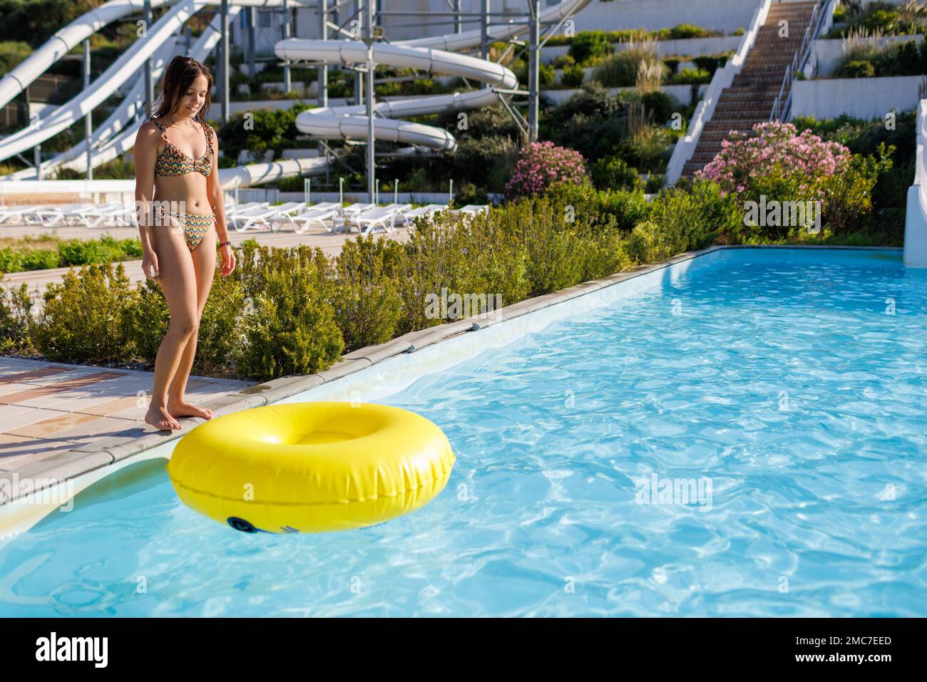 A teenage girl stands at the edge of the pool and throws a large inflatable ring in the water park Stock Photo
