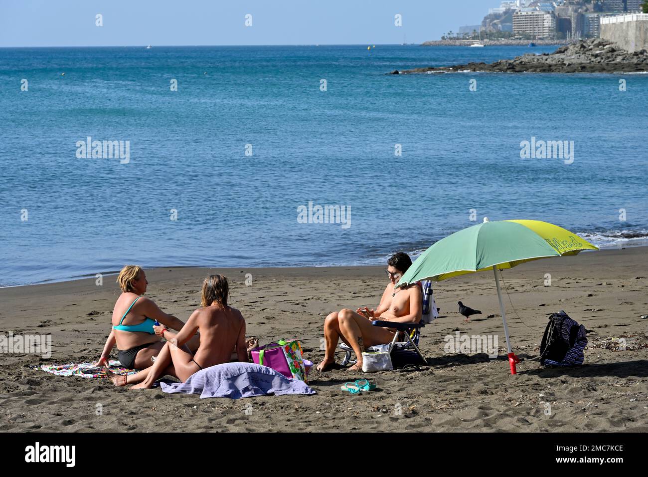 Three women sunbathing, relaxing on beach town of  Arguineguín, Gran Canaria, Canary Islands Stock Photo