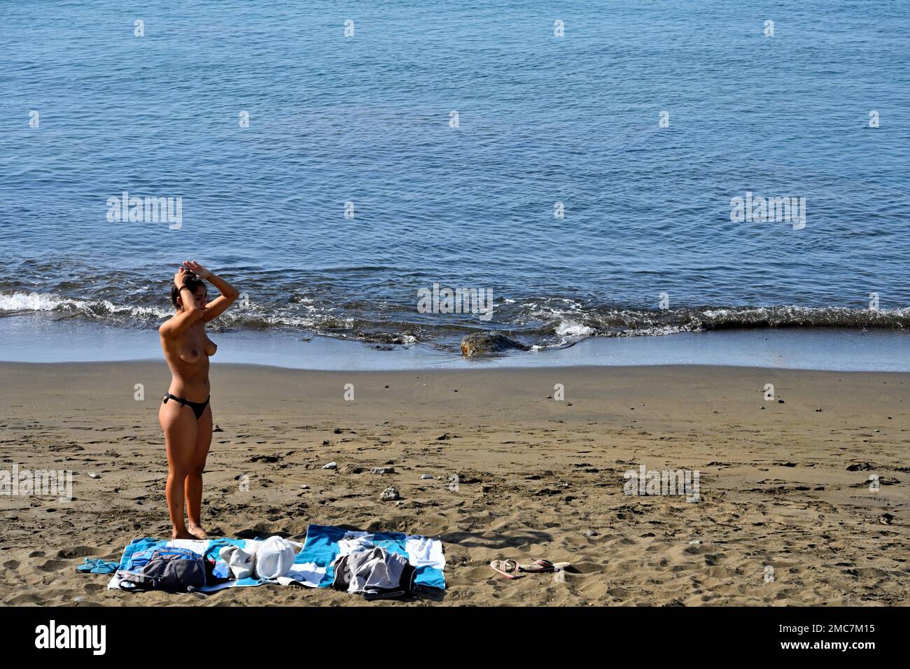Young woman on sandy beach by waters edge with sea and beach towels Stock Photo