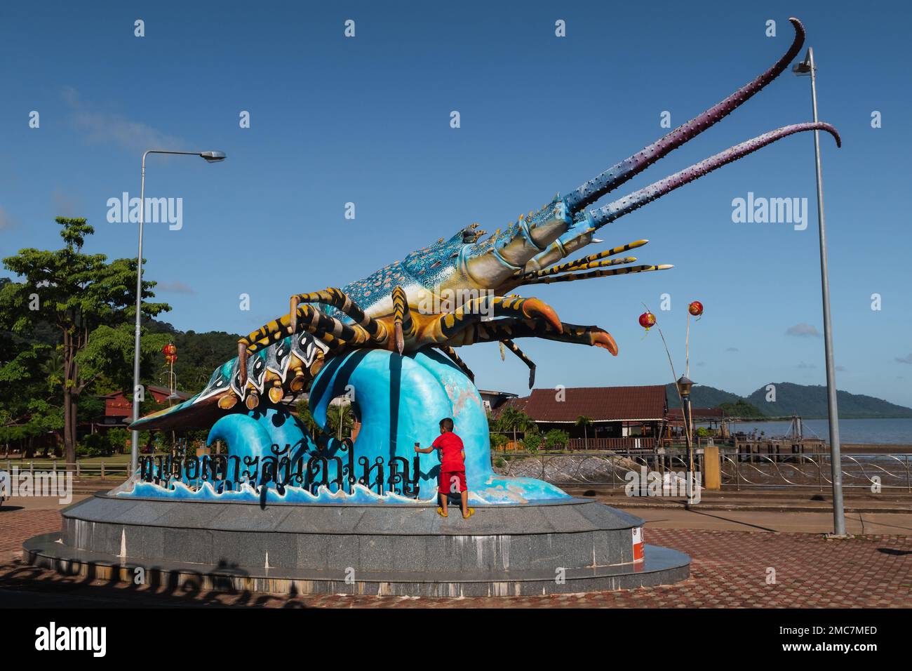 Lobster statue at the Old Town Koh Lanta pier, with child wearing red climbing on it. Ko Lanta