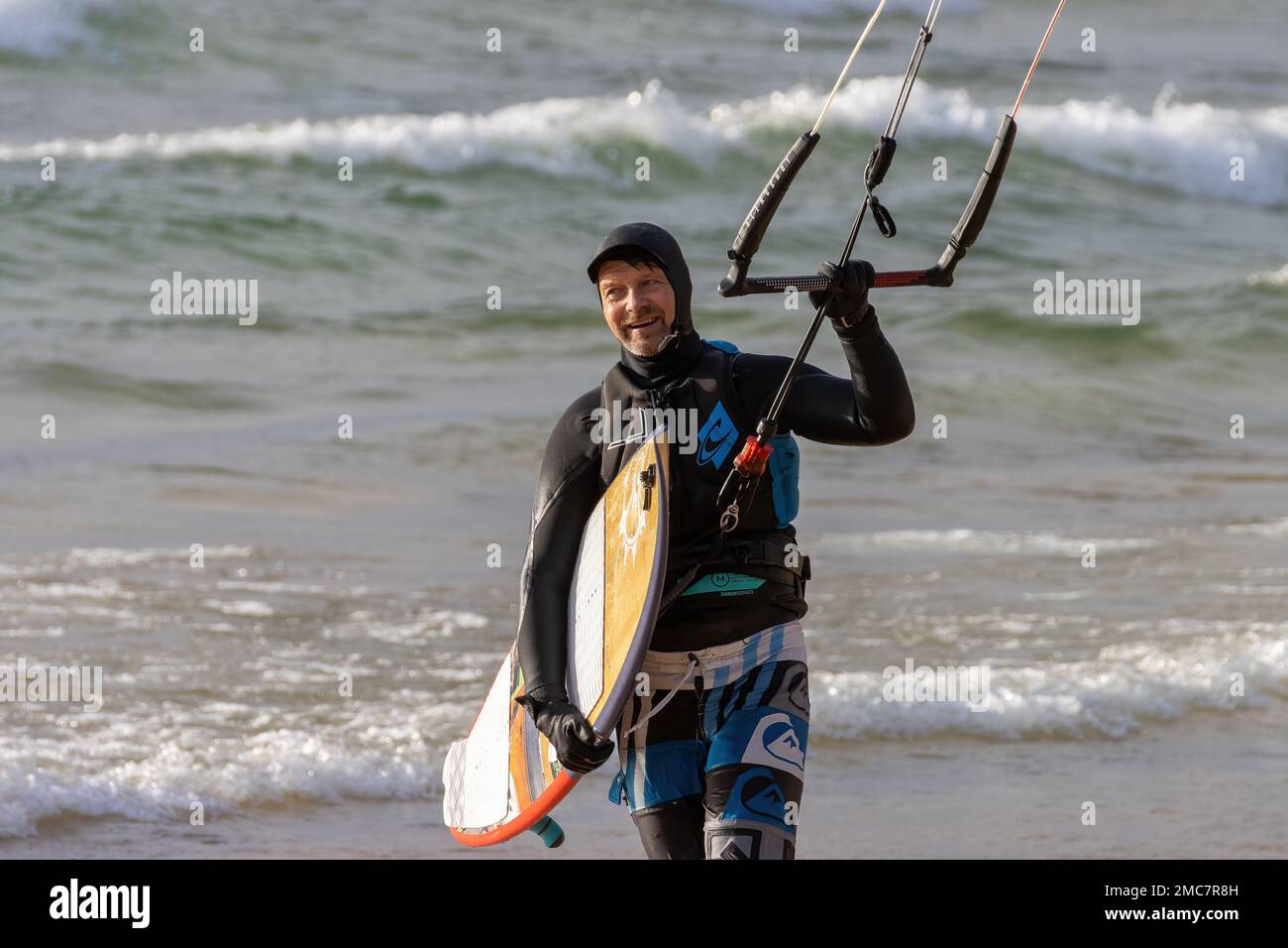 A surfer male holding a surfboard on the beach Windsurfing sail in