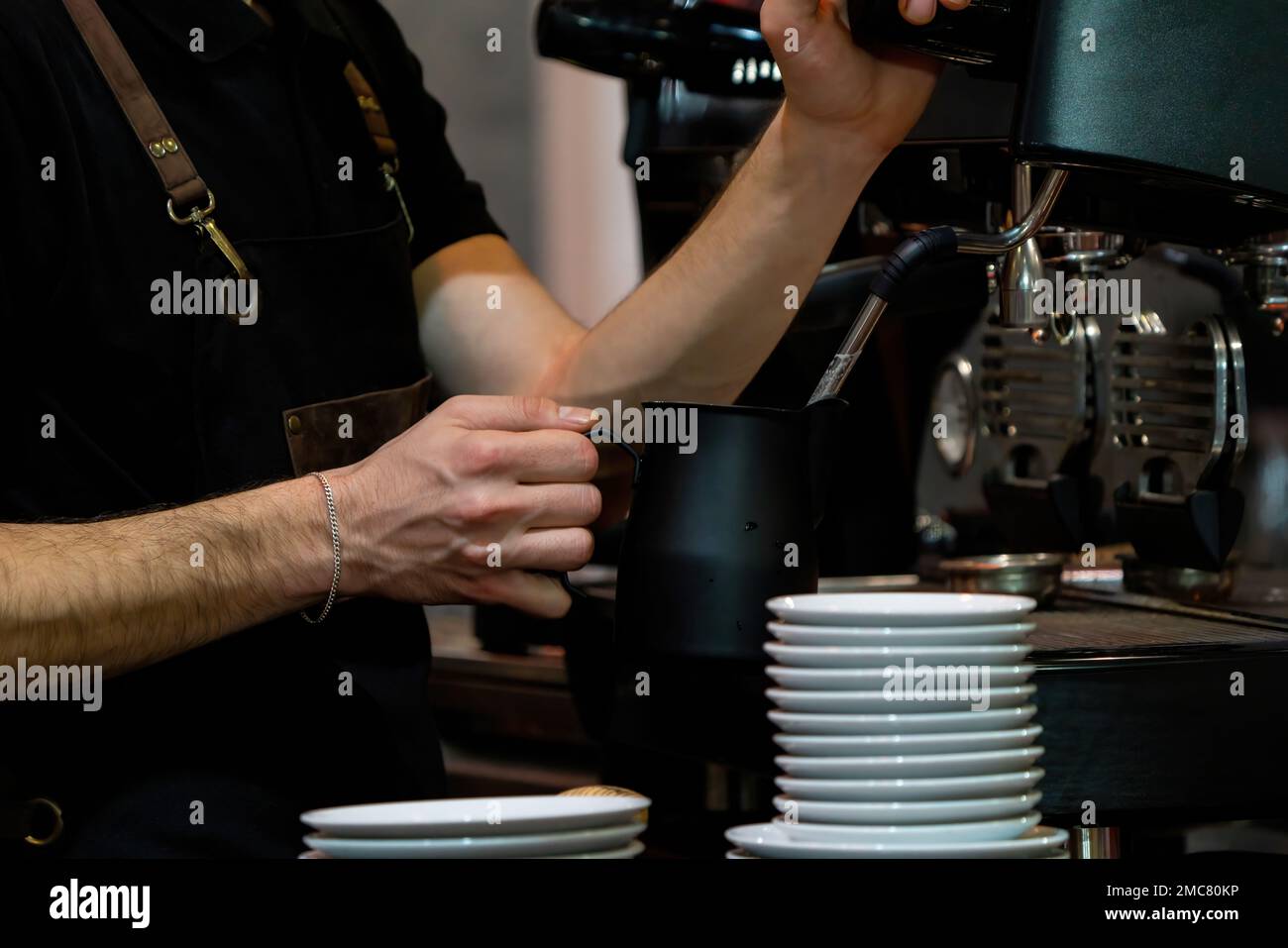 Barista frothing milk to make coffee. Barista hands in front of coffee machine Stock Photo