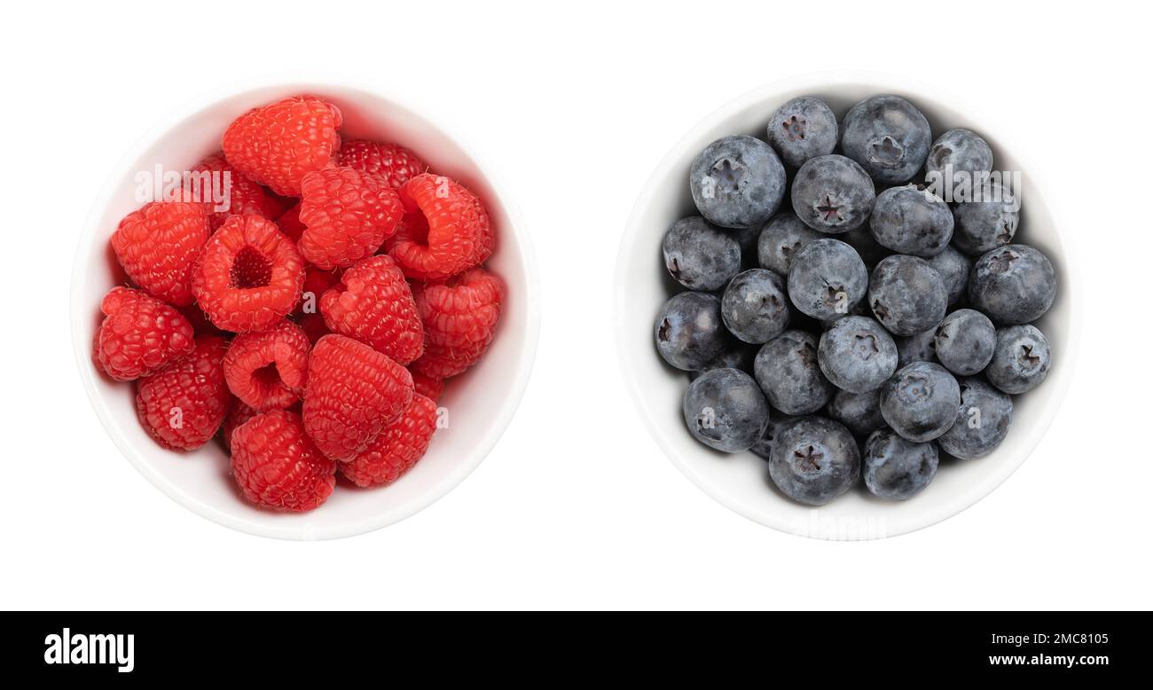 Fresh raspberries and blueberries, in white bowls, from above. Whole and ripe fruits. Stock Photo