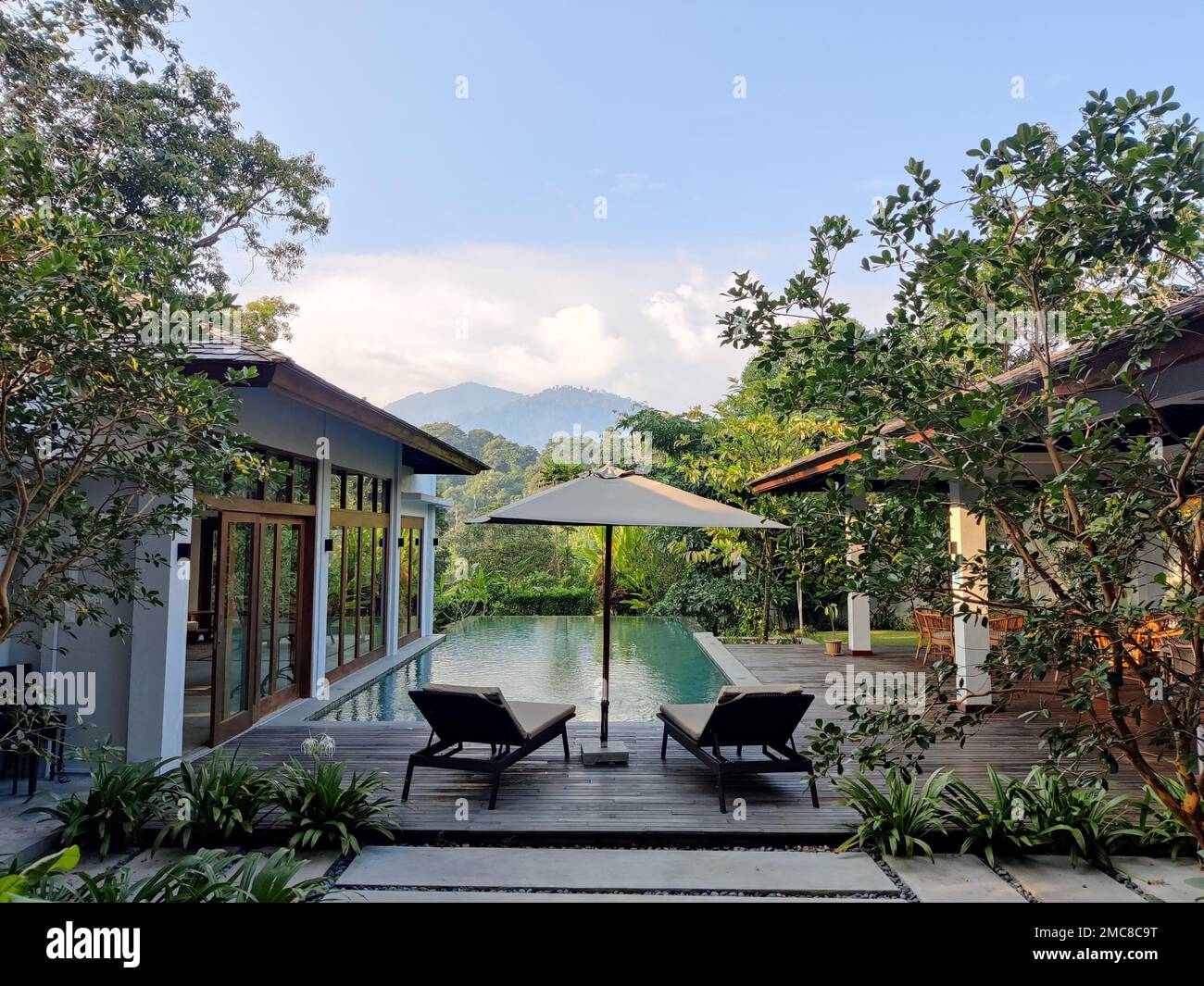 A quiet view of two Lounge Chairs by a pool with wooden houses and