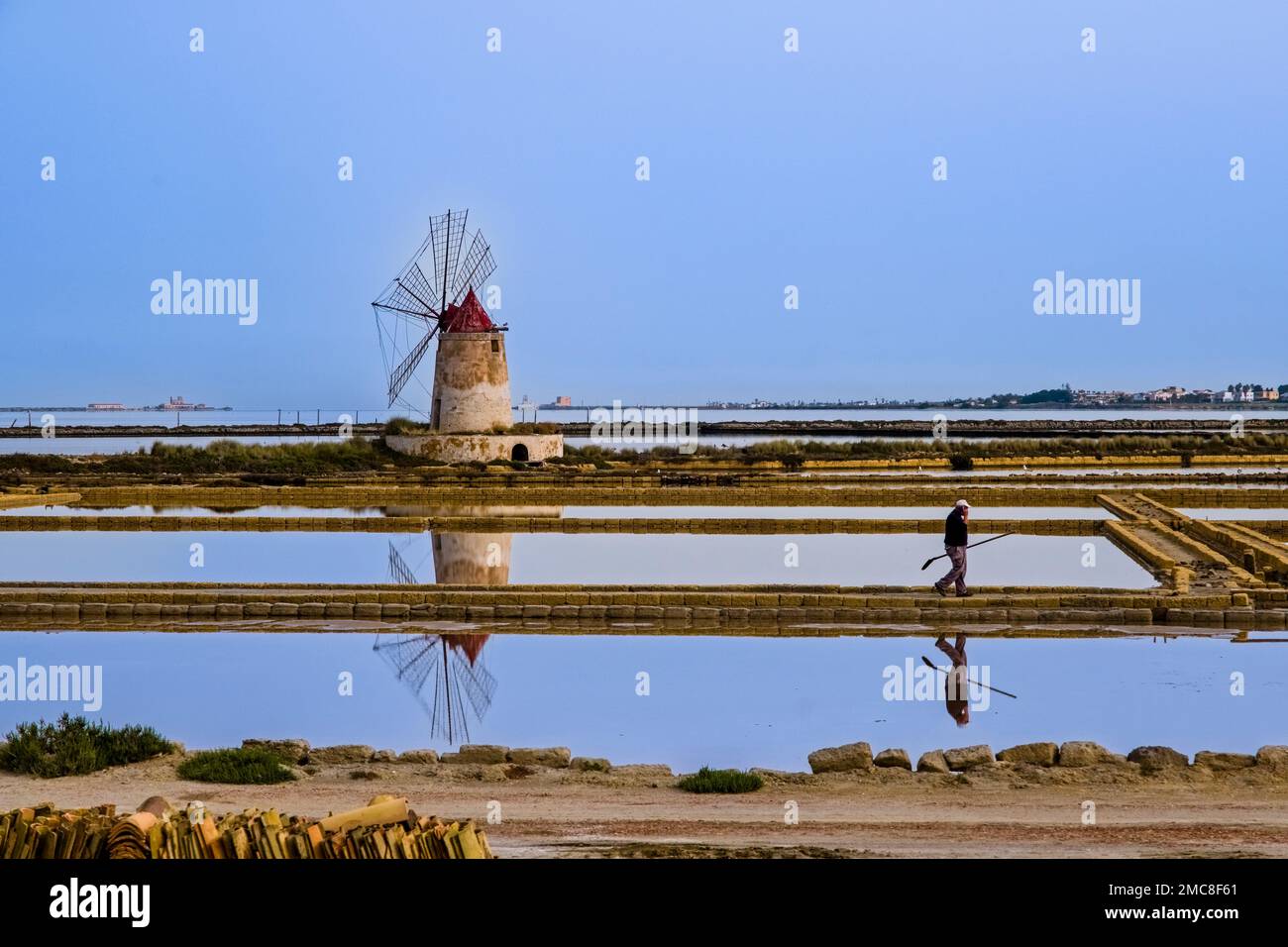 Water basins, salt pans and a windmill at Mozia salt works, a worker is walking on a dam. Stock Photo