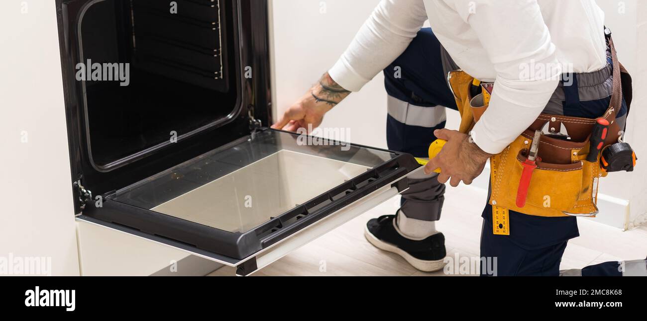 Professional serviceman repairing modern oven in kitchen Stock Photo