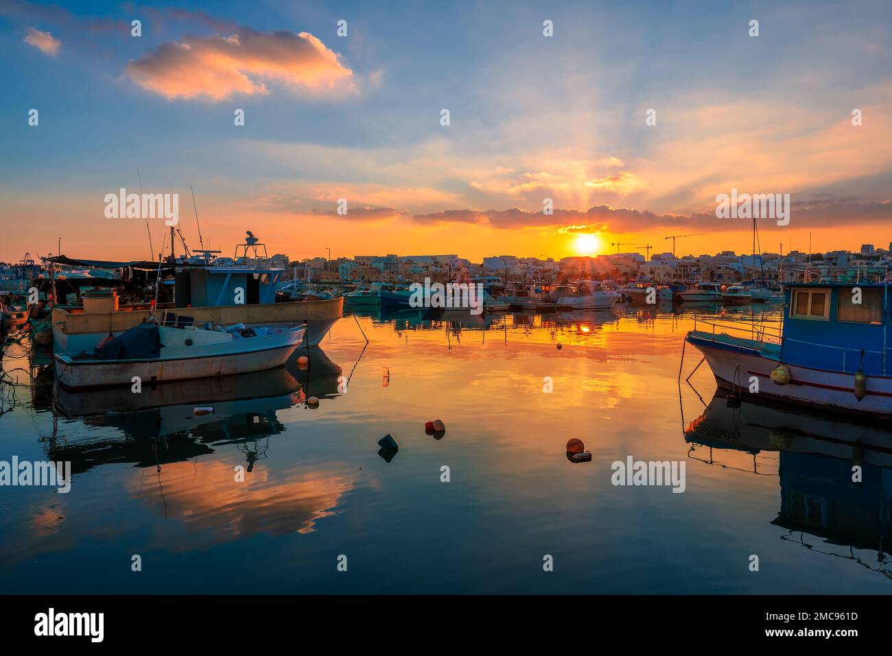 Beautiful colorful scene of a Village architecture and boats reflected in the sea, illuminated at sunset in Malta Stock Photo